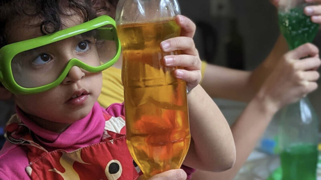Child wearing safety goggles holding a bottle with liquid.